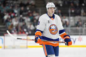 A man in white and blue jersey holding hockey stick.